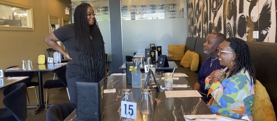 CheSa speaking with two people sitting at a table at her business: CheSa’s Bistro and Bar in Chicago, Illinois