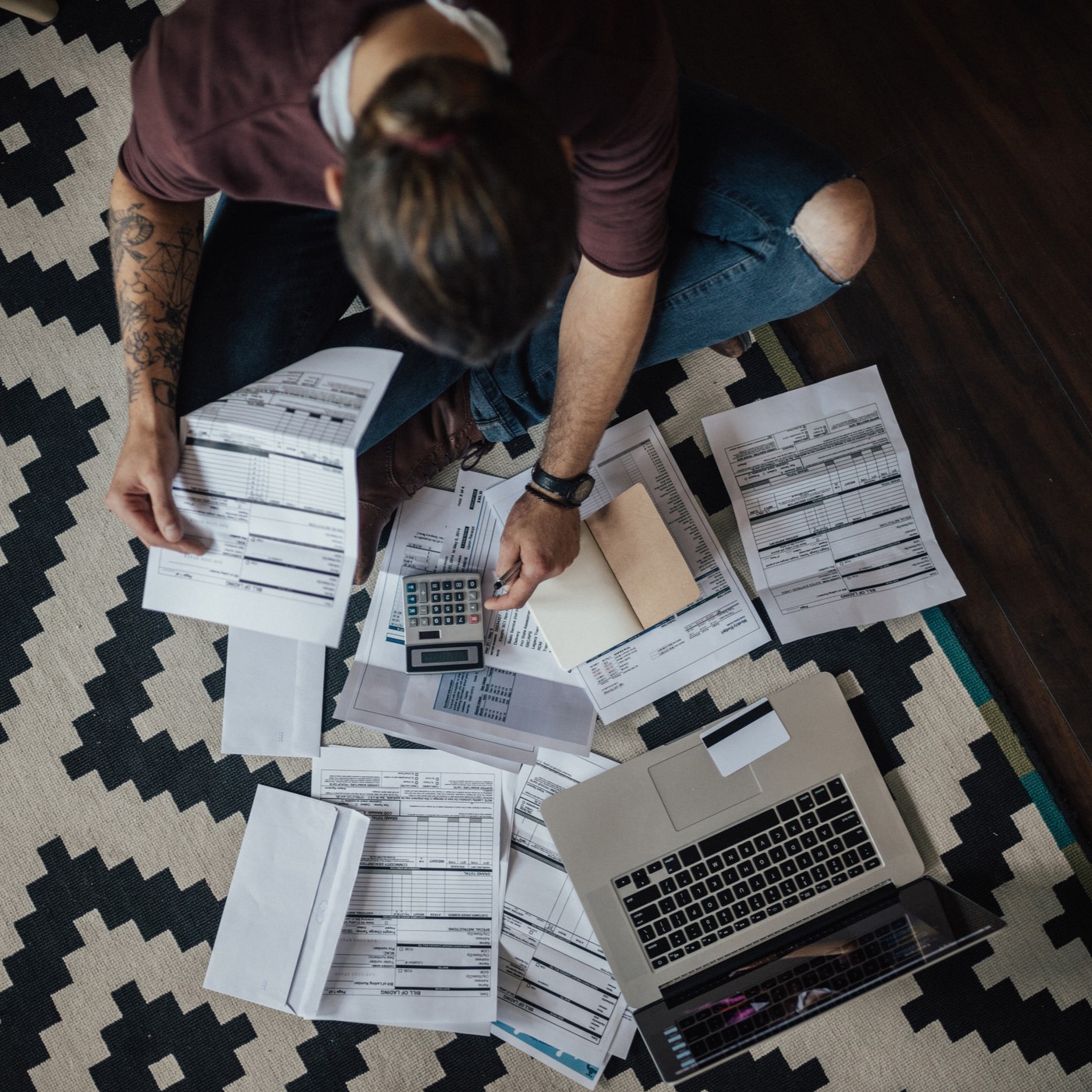 stressed person sitting on the floor with bills scattered in front of them