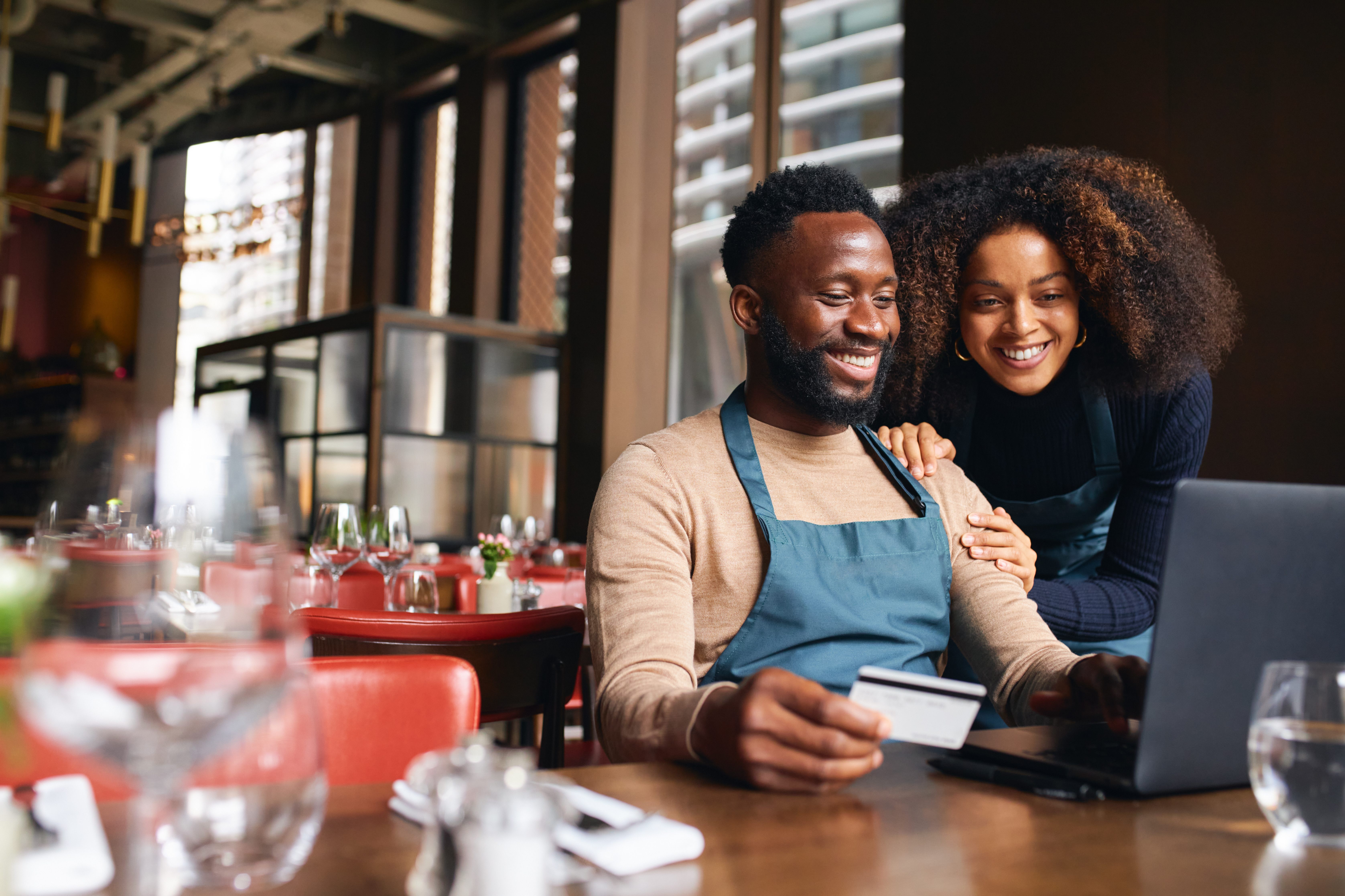 two happy people looking at a laptop smiling with one holding a credit card