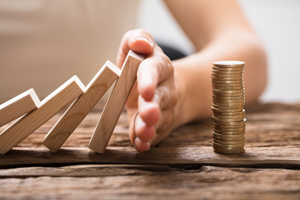 person using their hand to prevent a falling row of dominos from tipping over a stack on coins