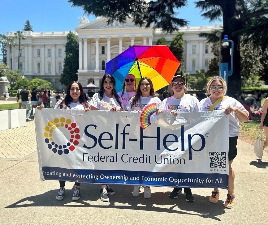 people holding a Self-Help Federal Credit Union banner in front of the California Capitol building