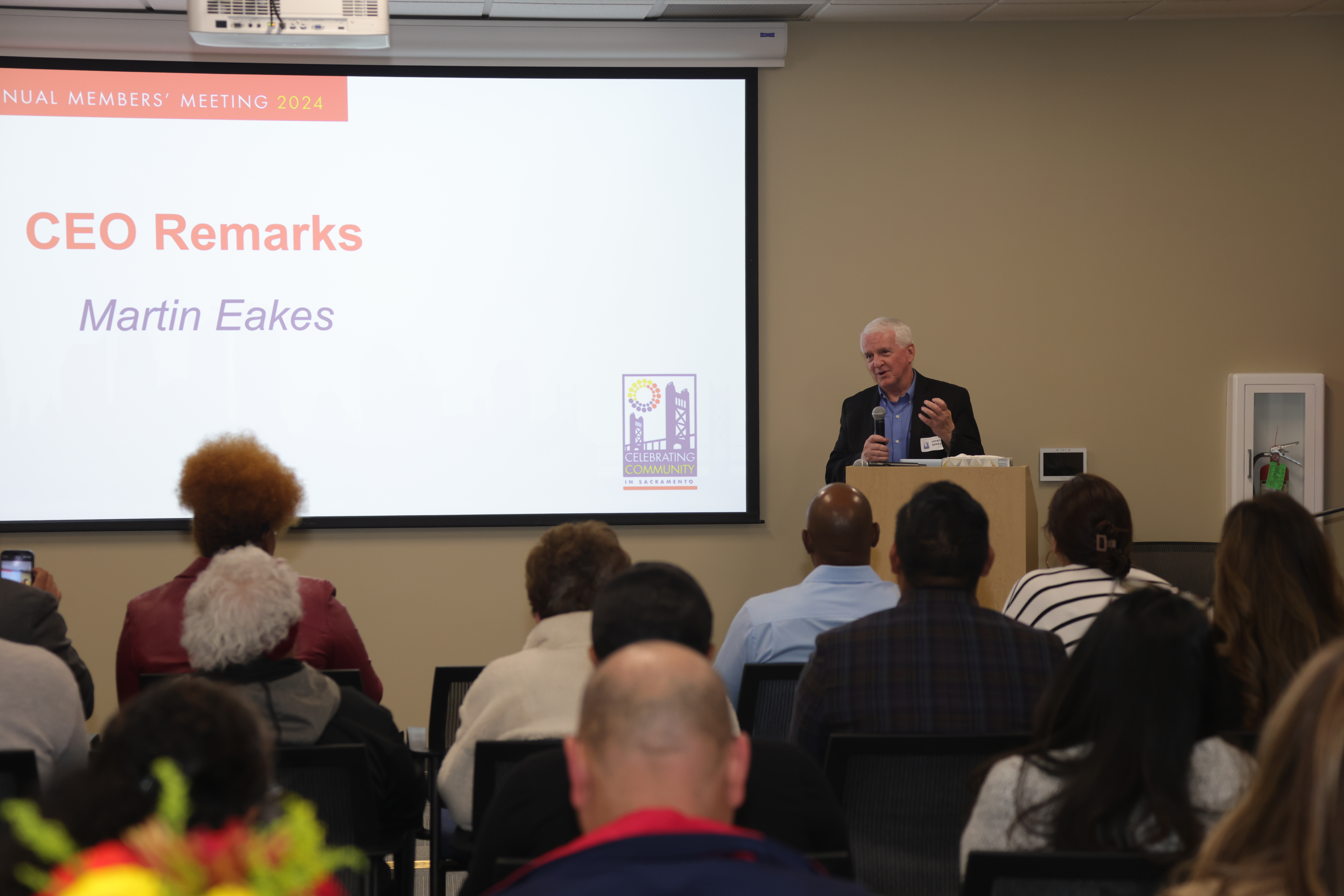 a photo of Self-Help Federal Credit Union's CEO, Martin Eakes, talking into a microphone behind a podium on a stage at Self-Help Federal Credit Union's Annual Members' Meeting in Sacramento, California.